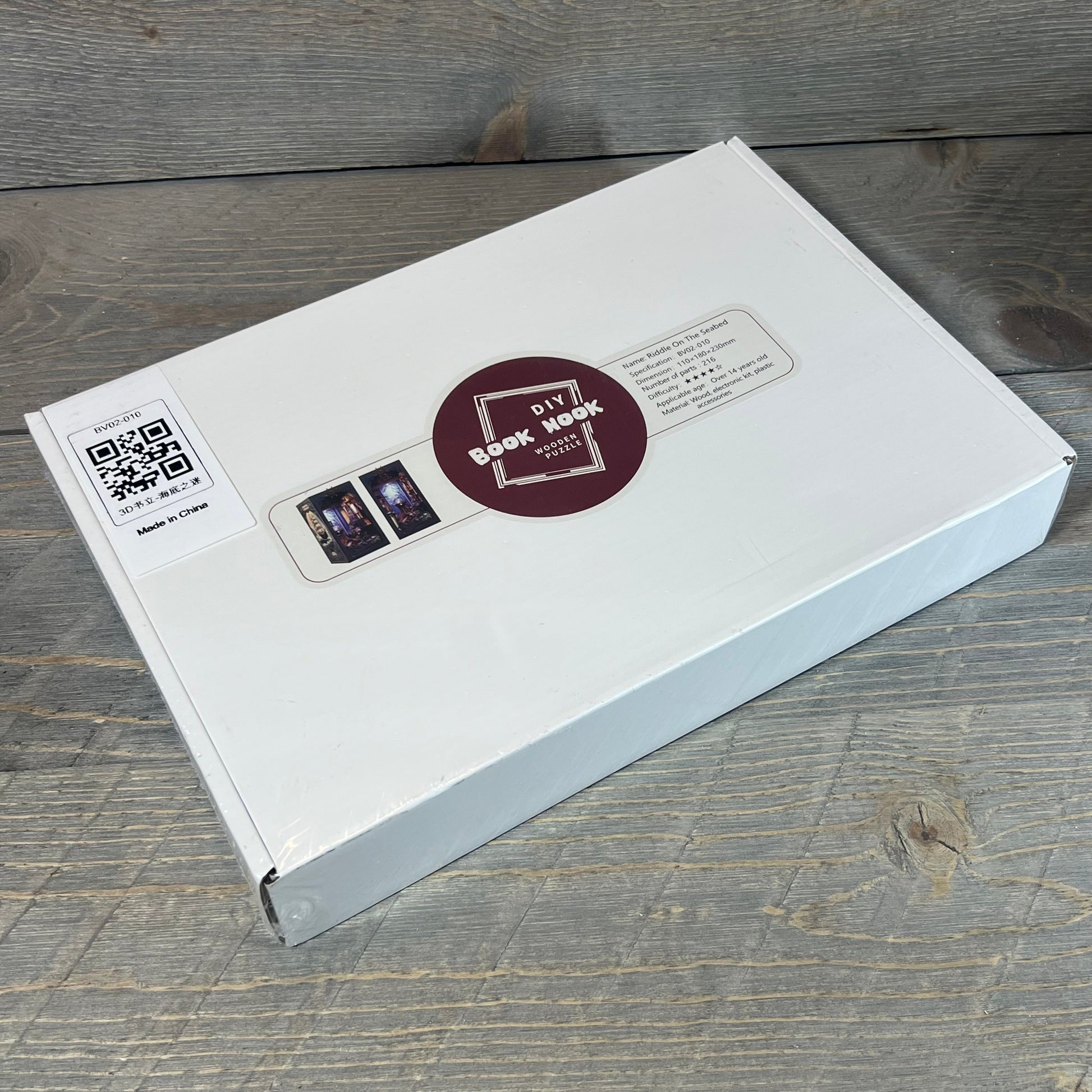 DIY Book Nook Kit packaging for Seabed Riddle with QR code and product details on a wooden surface.