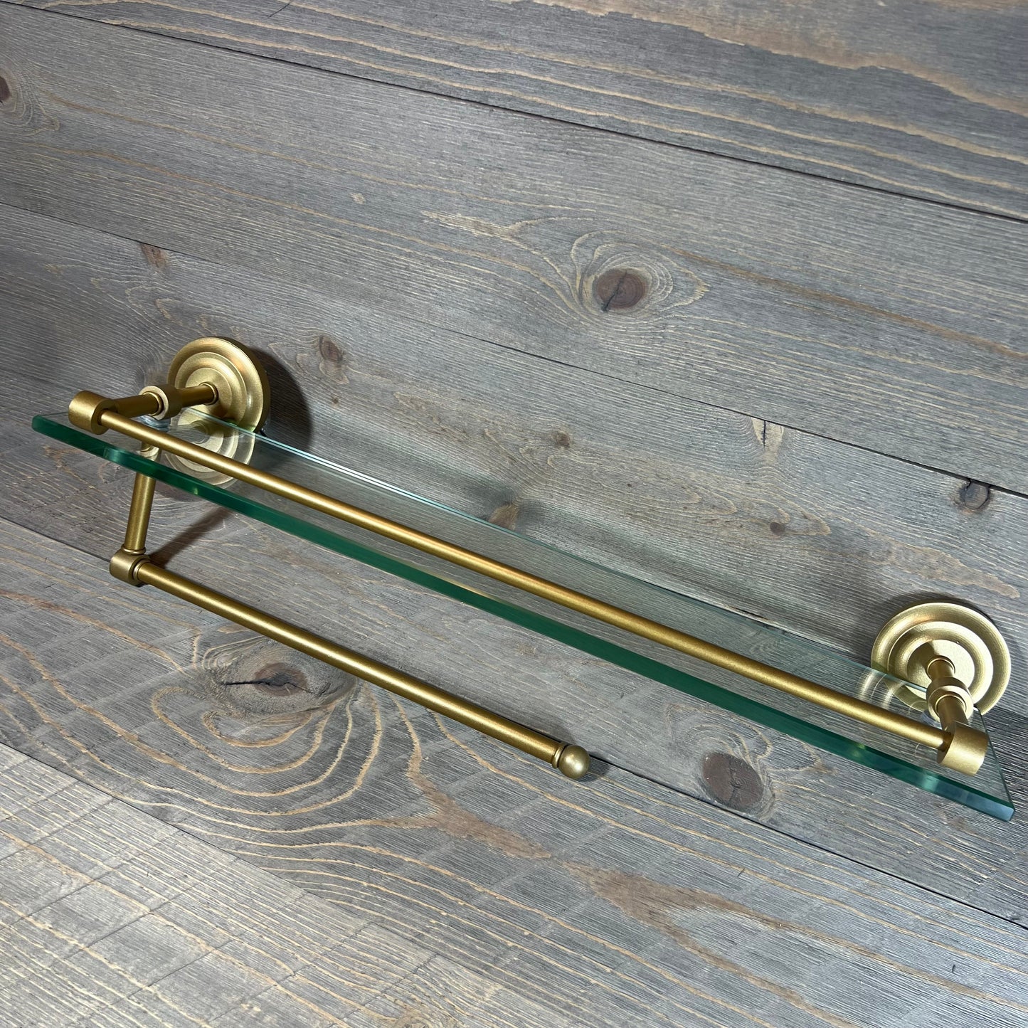 Elegant brass paper towel holder with 22" glass shelf on rustic wood background.