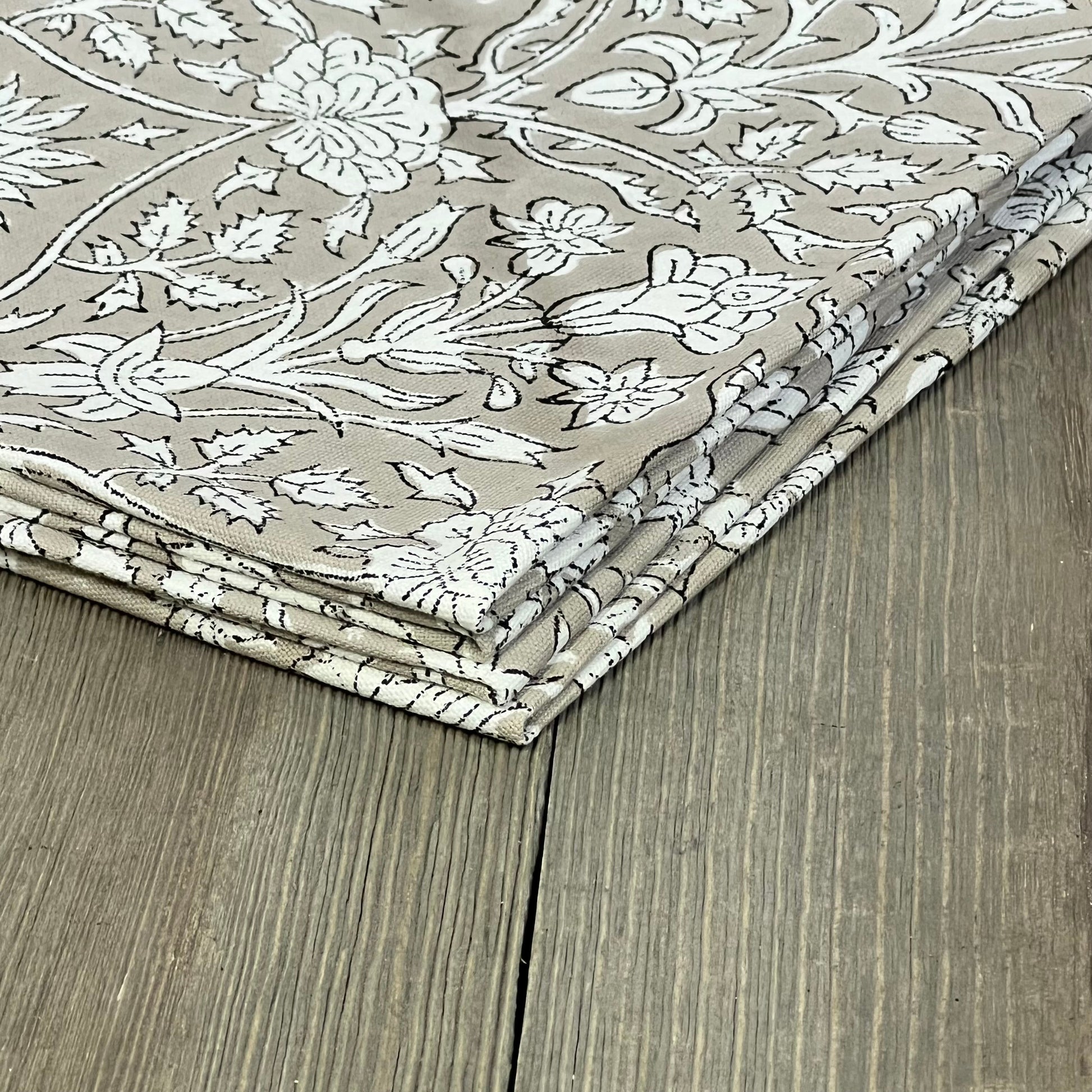 Boho round placemats with floral embroidery in taupe, stacked on wooden table, perfect for Easter dining decor.
