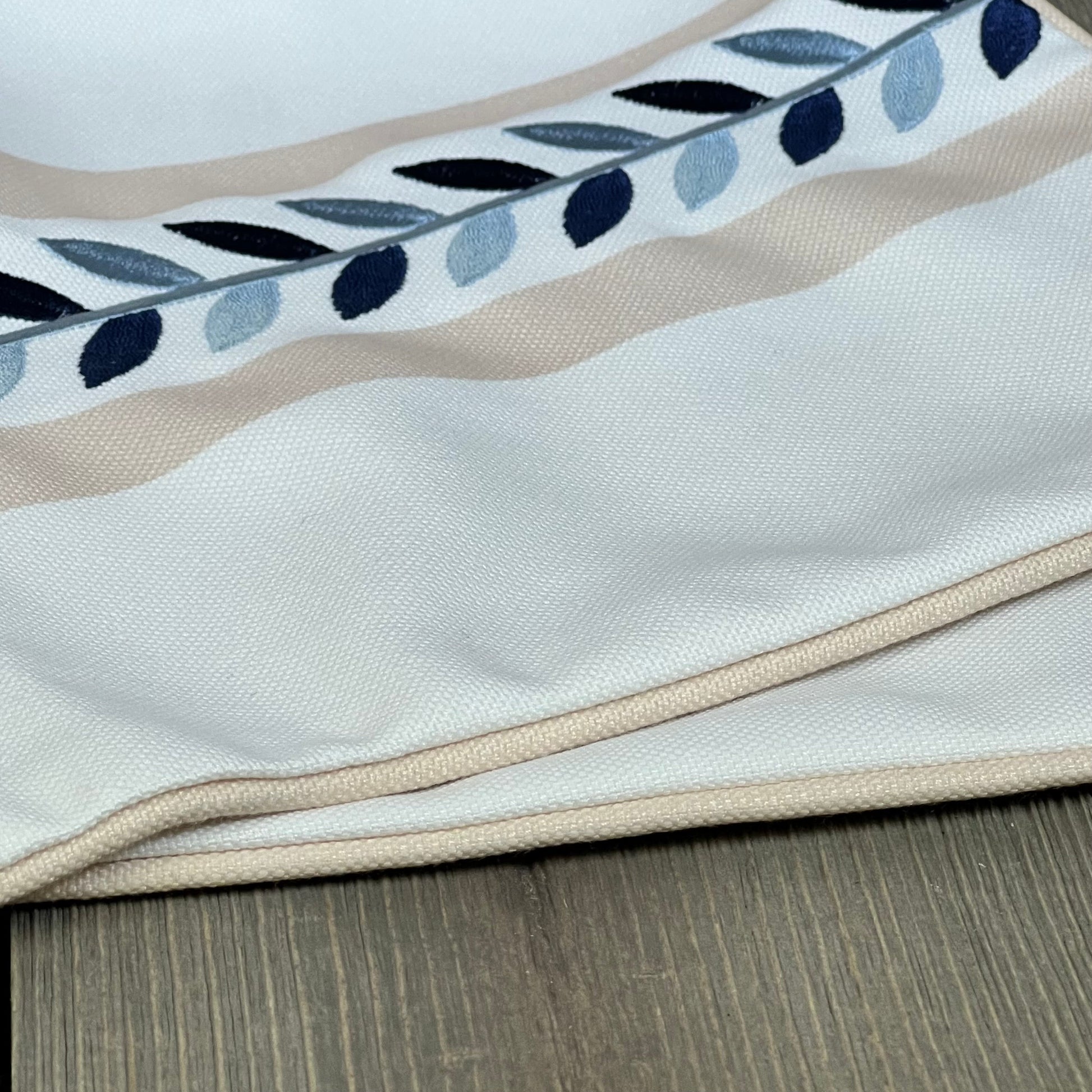 Coastal lumbar pillow cover with tan piping and embroidered leaf design, perfect for patios and couches. Water-repellent fabric.