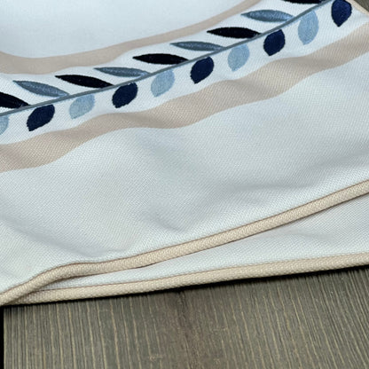Coastal lumbar pillow cover with tan piping and embroidered leaf design, perfect for patios and couches. Water-repellent fabric.