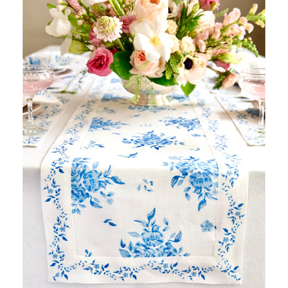Floral blue linen table runner on a dining table with elegant pink and white floral centerpiece, perfect for summer decor.