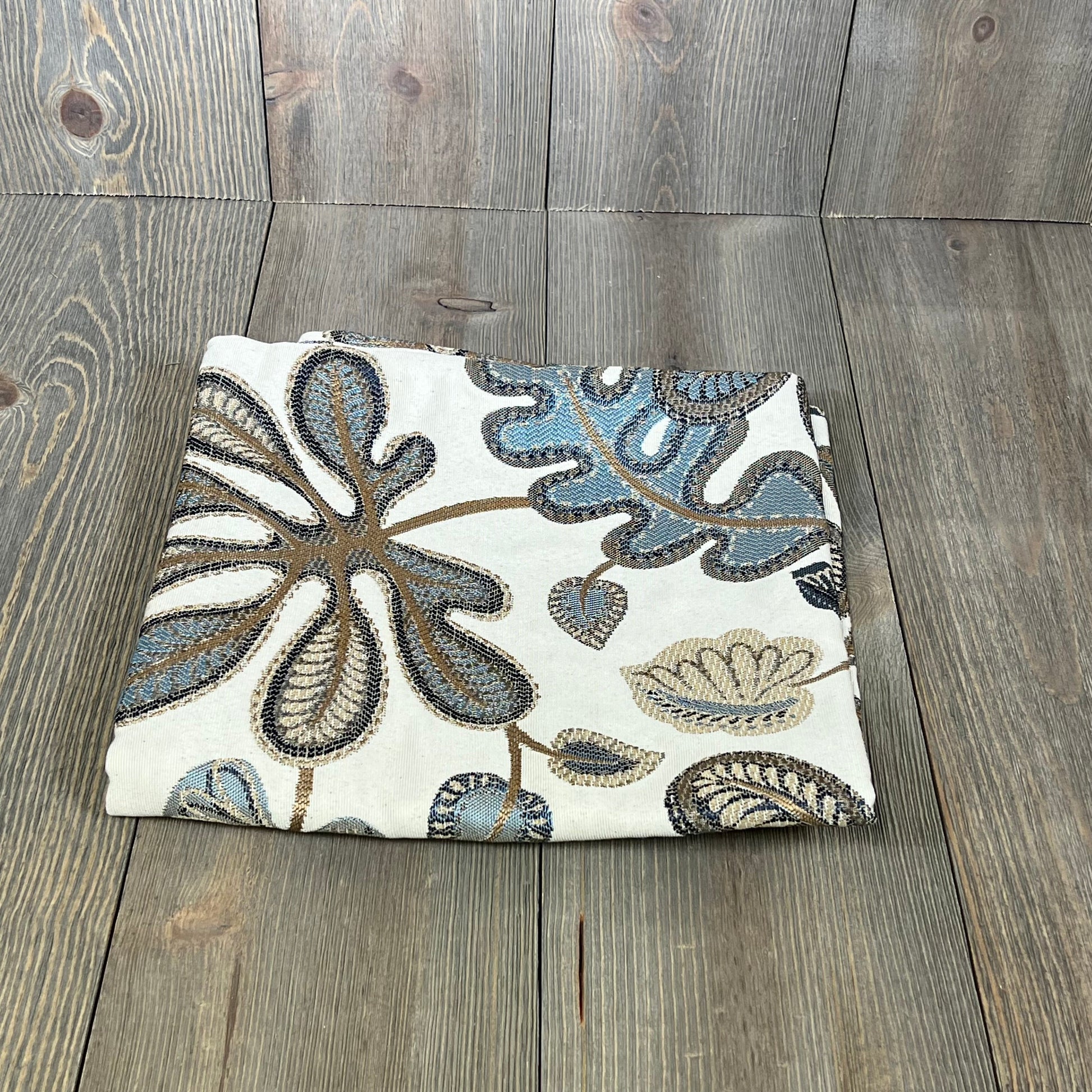 Jacquard tropical leaf pattern throw pillow cover in blue and cream, folded on a wooden surface, 20x20 inches.