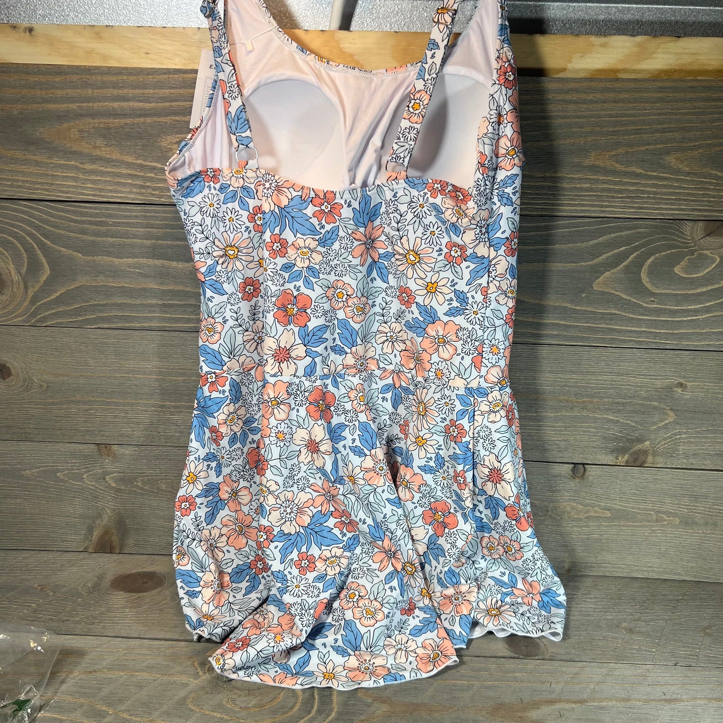 Floral swimdress with tummy control, featuring vibrant pink and blue flowers on a wooden background.