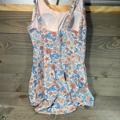 Floral swimdress with tummy control, featuring vibrant pink and blue flowers on a wooden background.