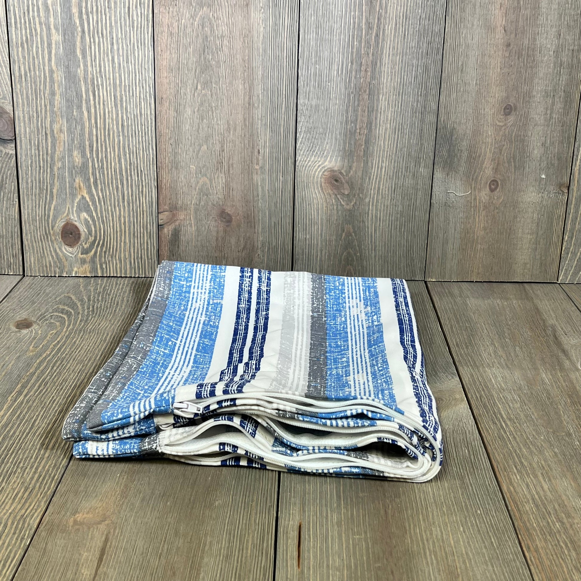Folded outdoor lumbar pillow covers in blue stripes on wooden surface, perfect for patio, garden, or balcony decor.