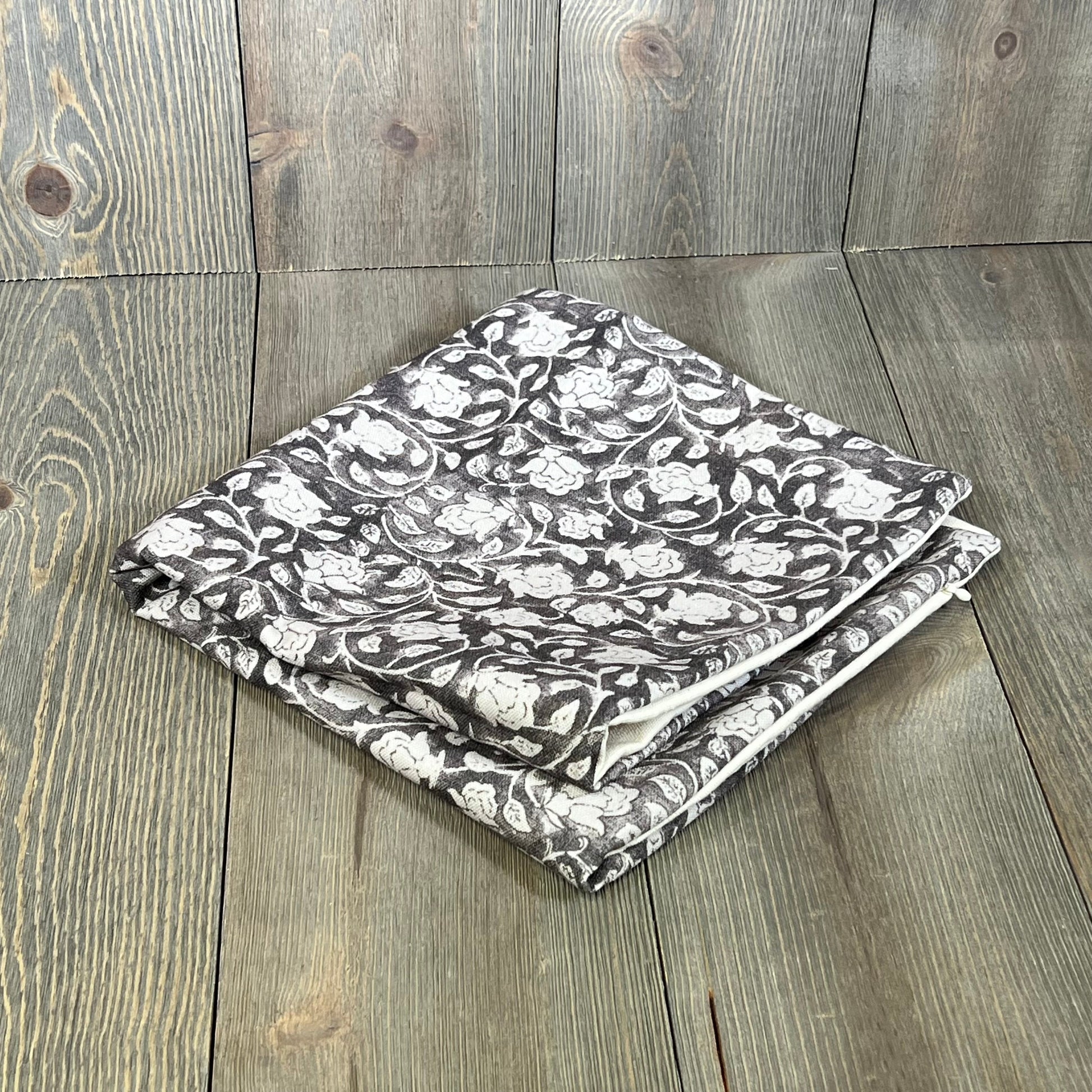Taupe floral pillow cover 20x20, folded on wood surface, enhancing couch decor with neutral floral accent.
