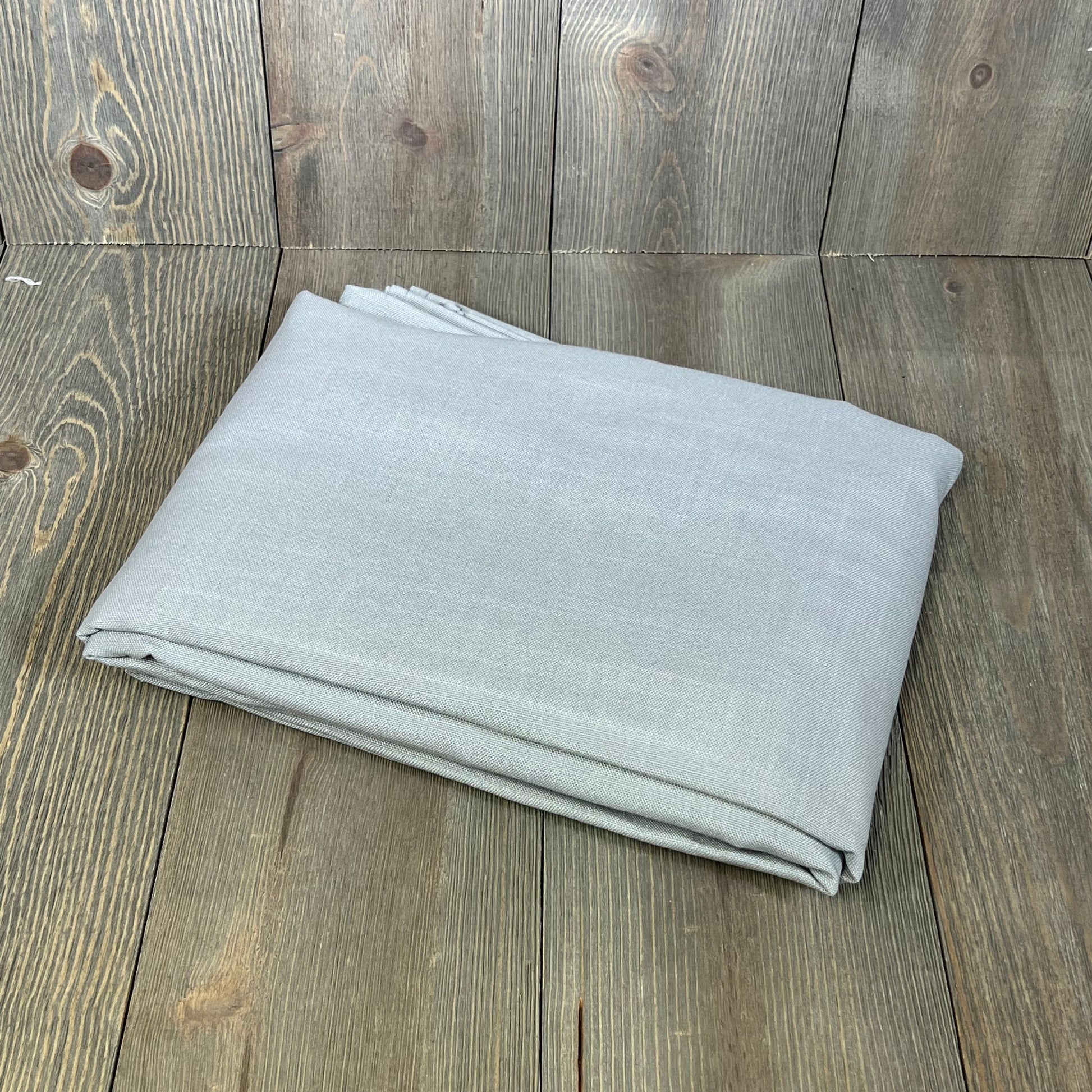 Folded grey linen textured tablecloth, 60 x 104 inches, on rustic wooden surface; premium, wrinkle-free, spill-proof fabric.