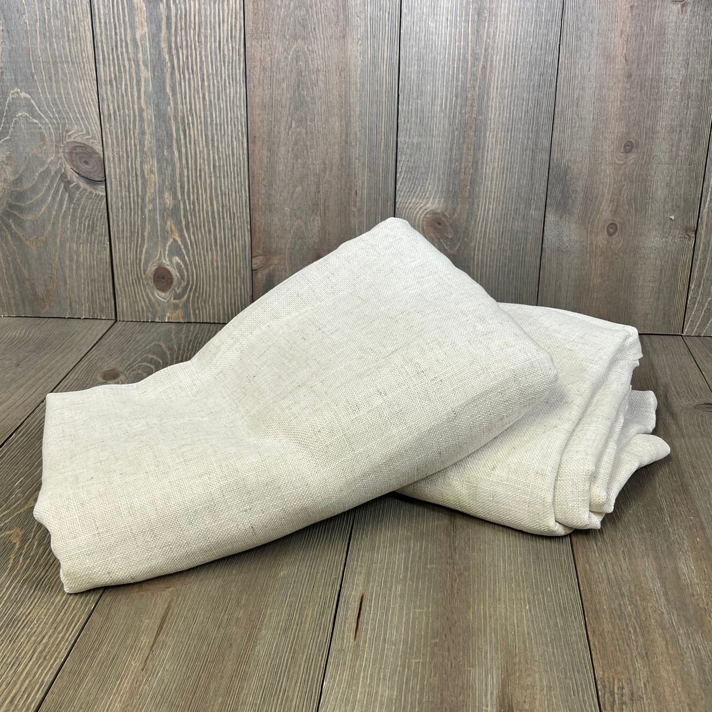 Natural linen curtains folded on wooden floor, showcasing semi-sheer fabric with light filtering for bedroom and living room.