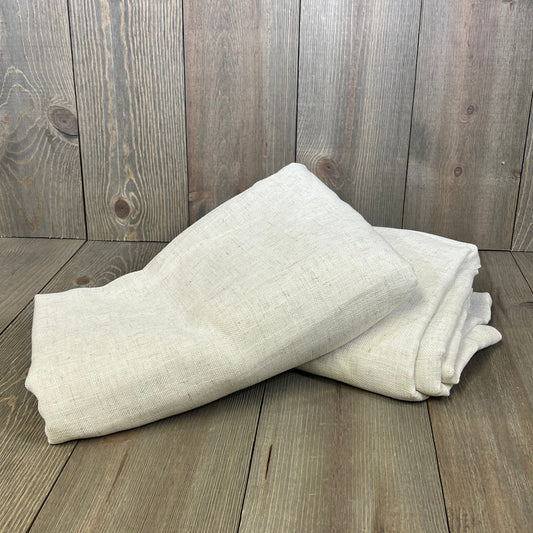 Natural linen curtains folded on wooden floor, showcasing semi-sheer fabric with light filtering for bedroom and living room.
