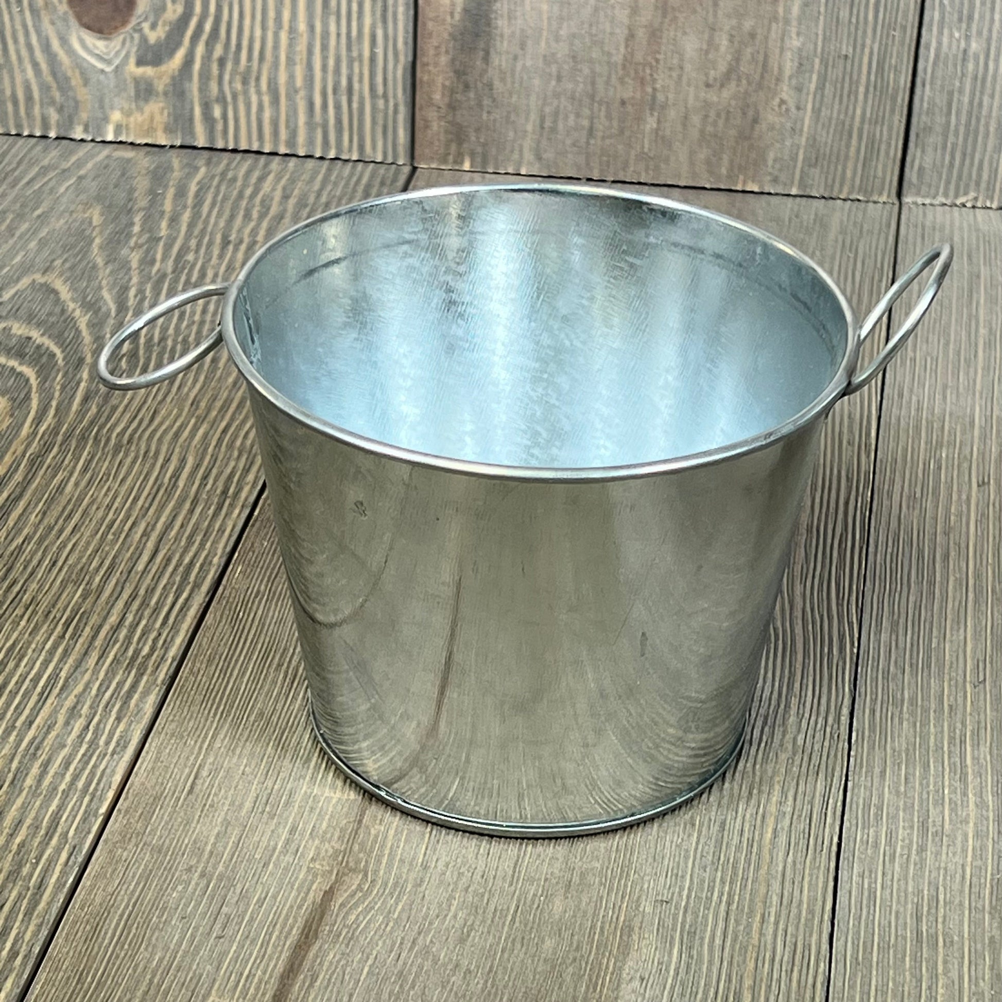 Mini galvanized bucket with handles on rustic wooden background, ideal for crafts and home decor, 4.5 x 3.5 inches.