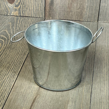 Mini galvanized bucket with handles on rustic wooden background, ideal for crafts and home decor, 4.5 x 3.5 inches.