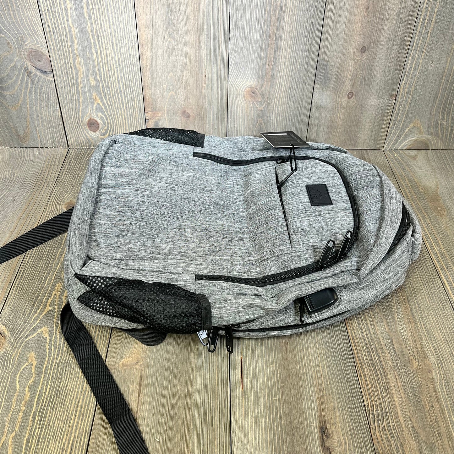 Grey MATEIN travel laptop backpack on wooden floor, featuring anti-theft design and USB charging port.
