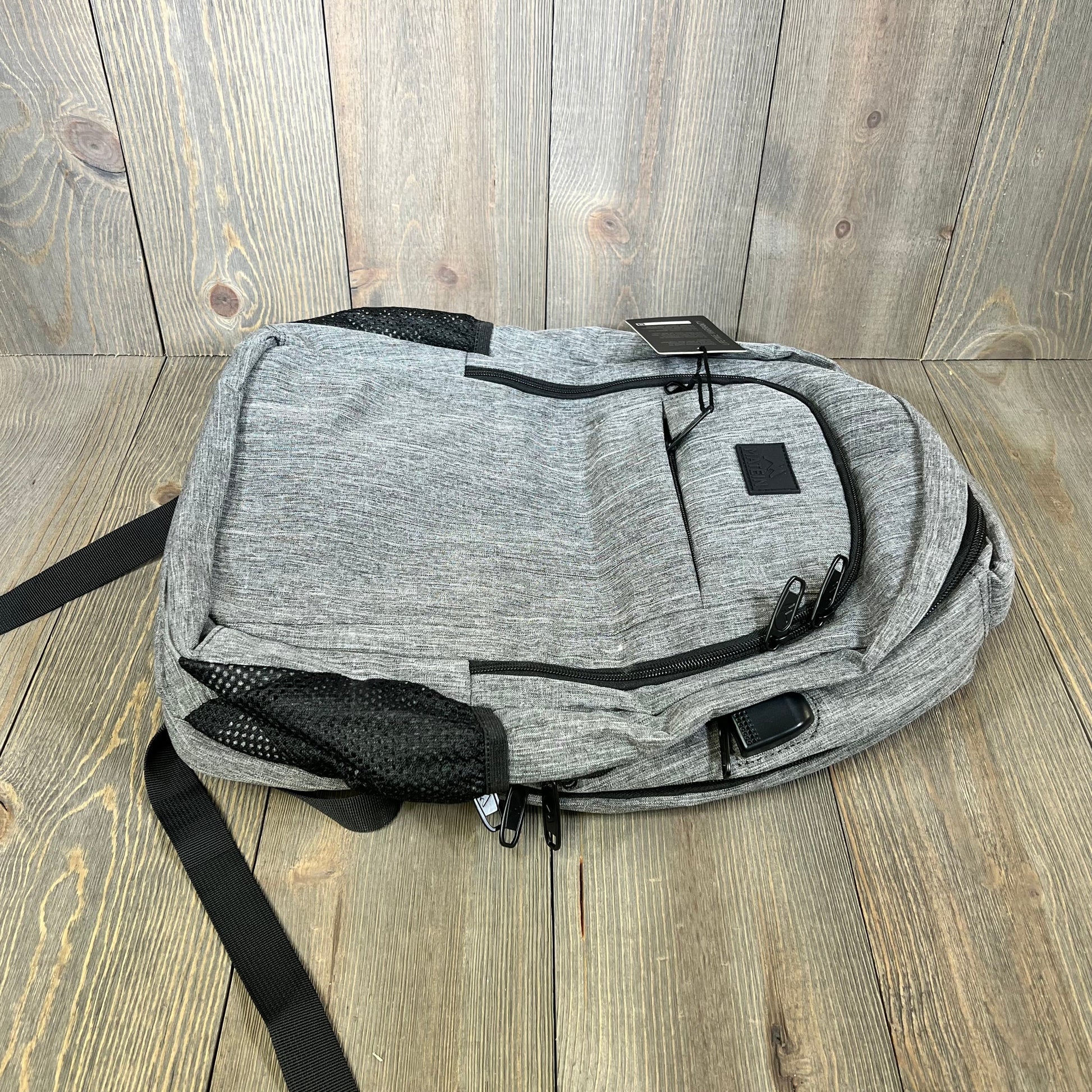 Grey MATEIN travel laptop backpack on wooden floor, featuring anti-theft design and USB charging port.