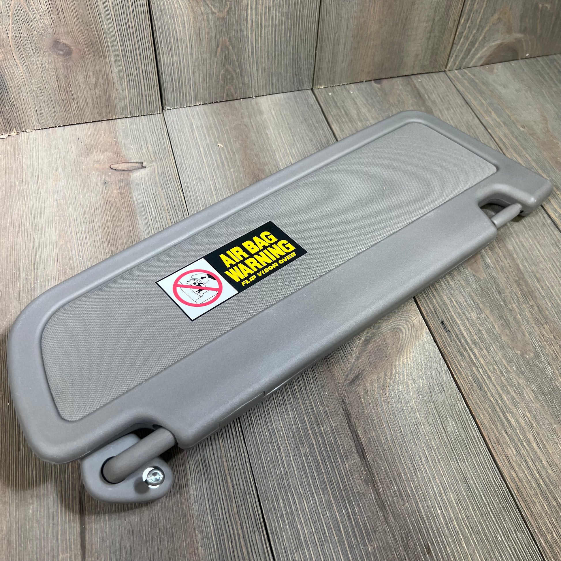Gray Dorman 74439 driver side sun visor for select Honda models, featuring airbag warning label, on wooden surface.
