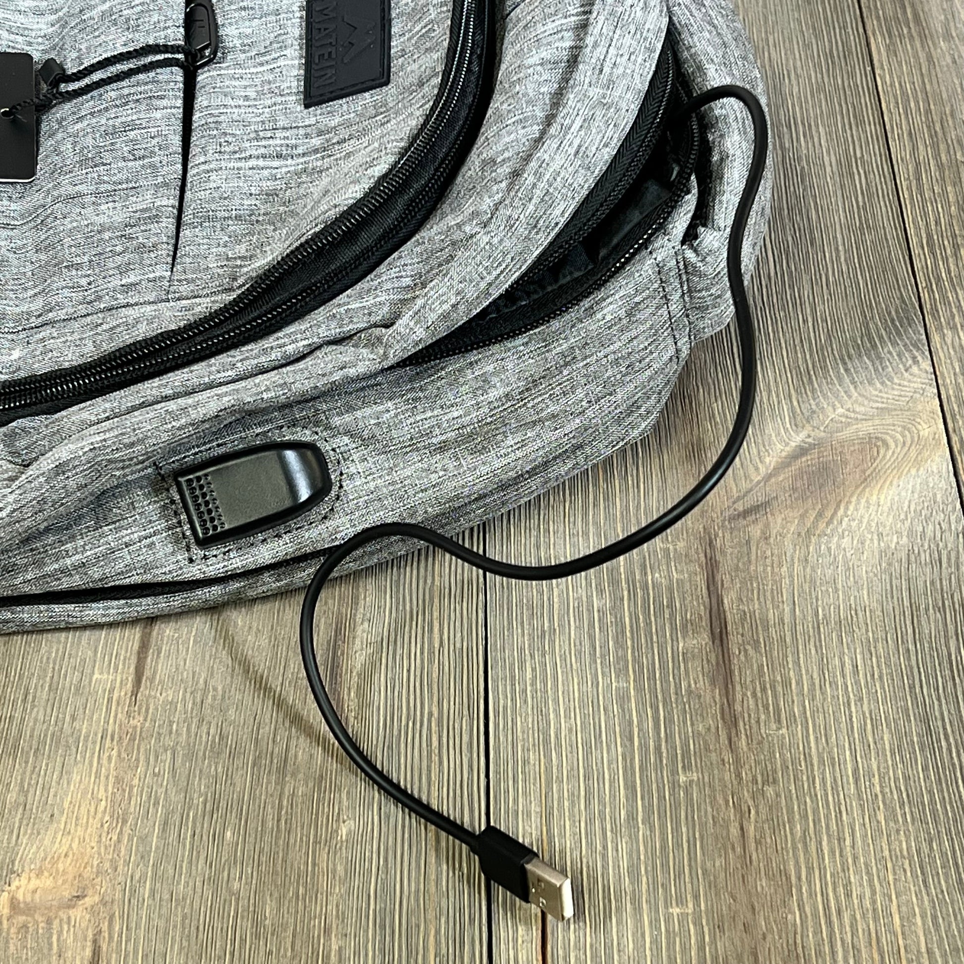 Grey MATEIN travel laptop backpack with USB charging port, highlighting durable fabric and sleek design on wooden floor.