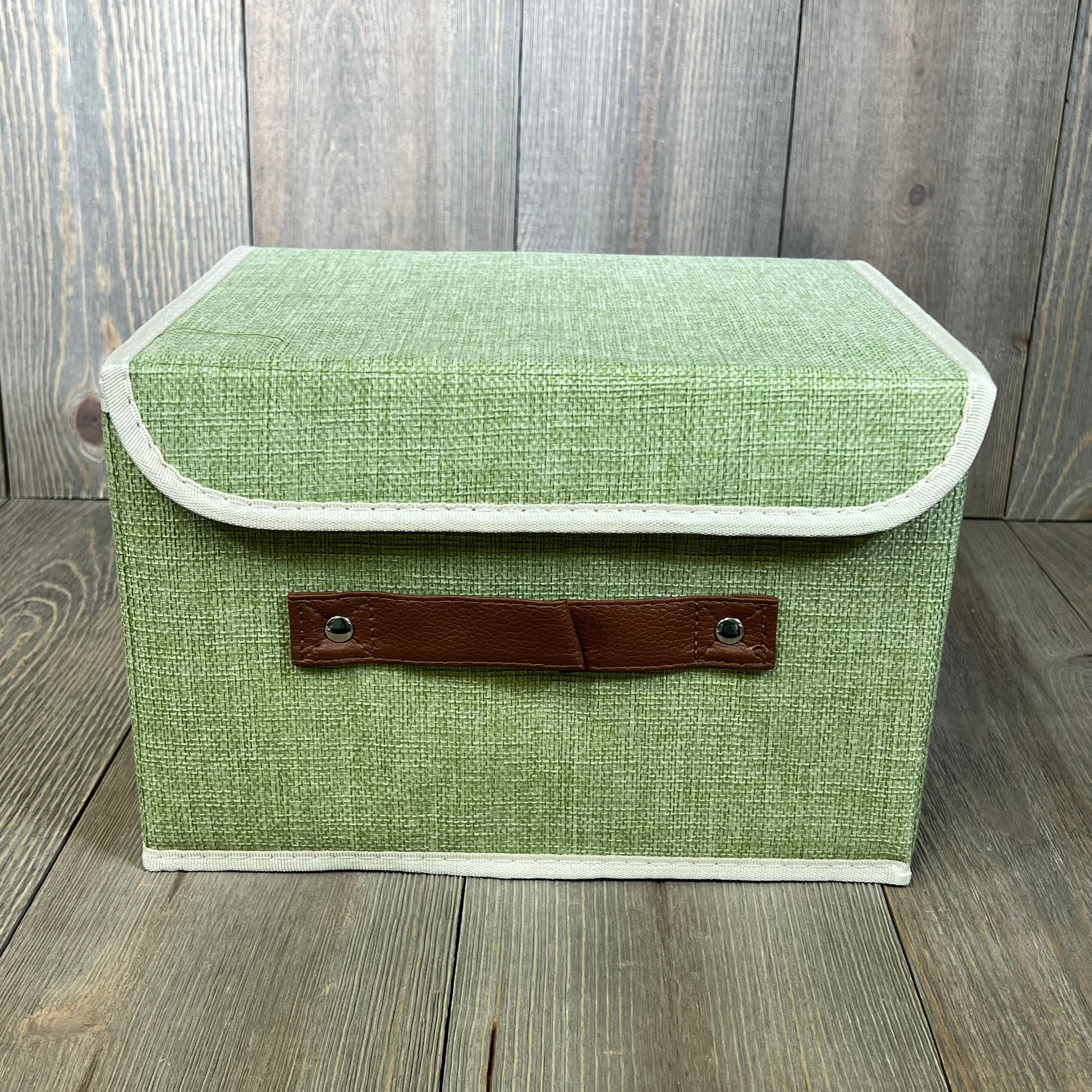 Green cotton linen storage box with lid, featuring faux leather handles. Ideal for organizing shelves and closets.