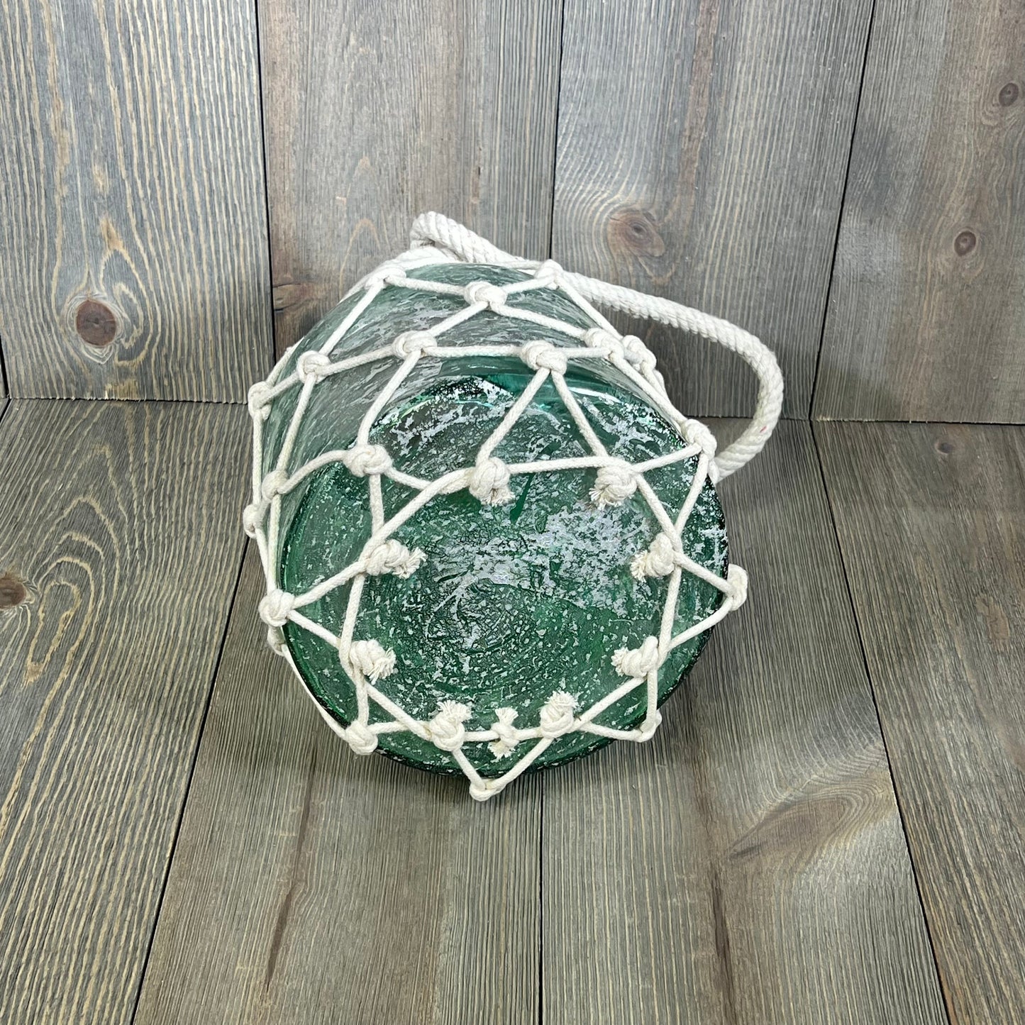 Blue glass cylinder lantern with white rope netting, perfect for coastal decor. Measures 7" x 7" x 15", available in a pack of 8.