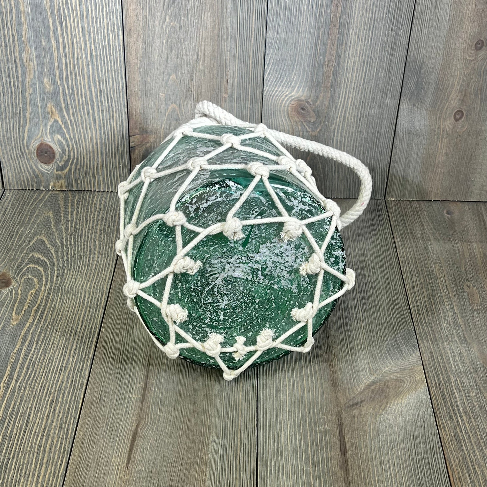 Blue glass cylinder lantern with white rope netting, perfect for coastal decor. Measures 7" x 7" x 15", available in a pack of 8.