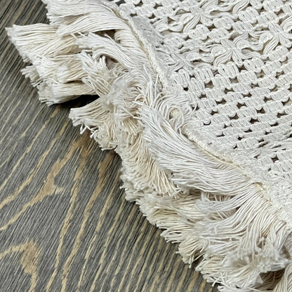 Cream beige macrame table mat with tassels on a wooden surface, showcasing intricate cotton linen weave, 12x20 inches.