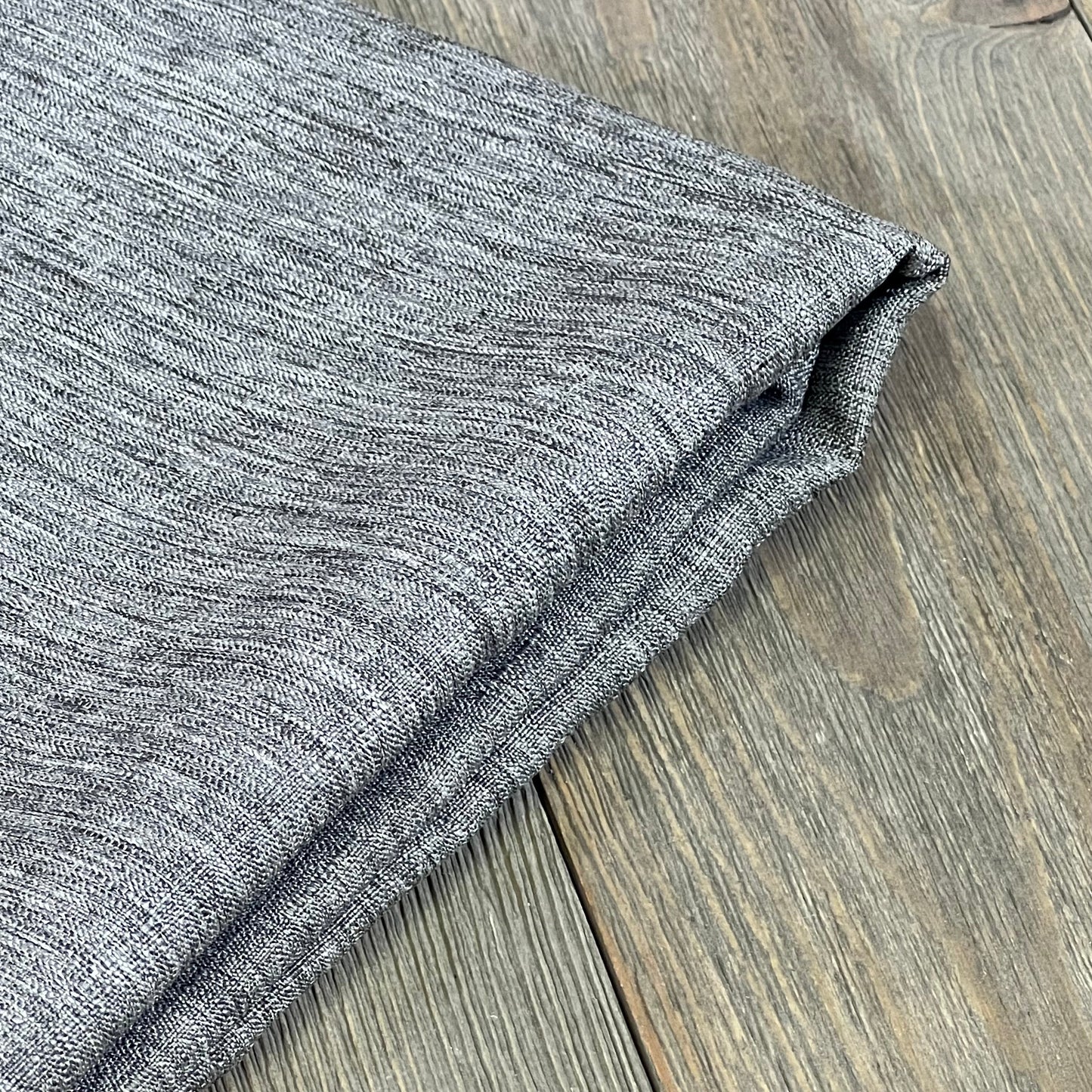 Grey textured linen tablecloth folded on wooden surface, showcasing wrinkle-free, waterproof material for dining decor.