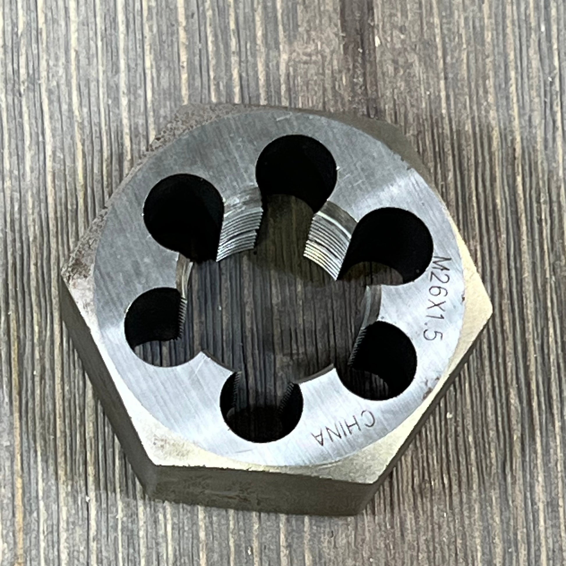Drill America DWTSMH26X1.5 carbon steel hex rethreading die, showcasing M26 X 1.5 threading against a wooden backdrop.