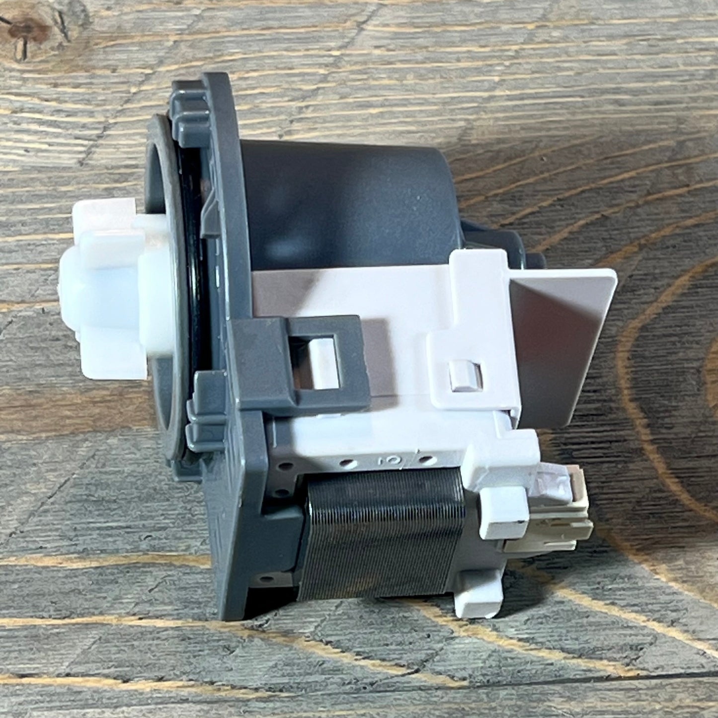 Kenmore Frigidaire dishwasher drain pump assembly on a wooden surface, showcasing its side profile and connector details.