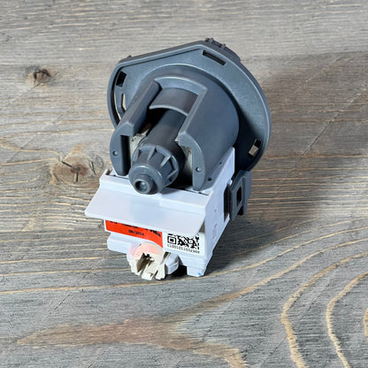 Kenmore Frigidaire dishwasher drain pump assembly on wooden surface, showcasing compact design and connection ports.