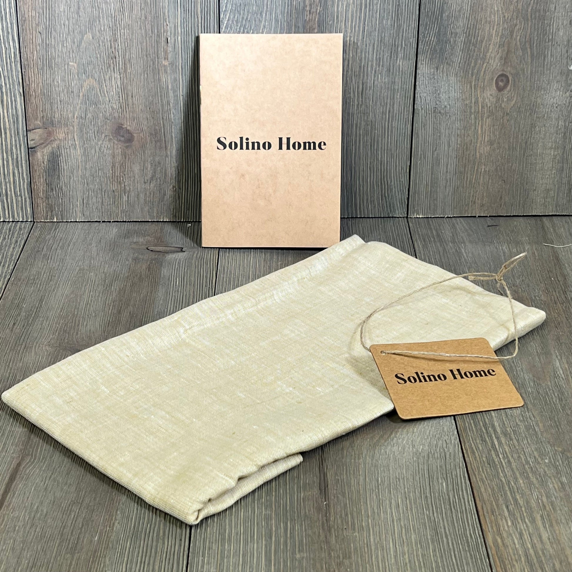 Champagne beige linen table runner by Solino Home, folded, with tag on wooden surface, ideal for dressers and coffee tables.