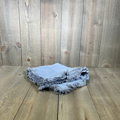 Light blue throw pillow covers with fringe and tassels, perfect for boho farmhouse decor, folded on a wooden surface.