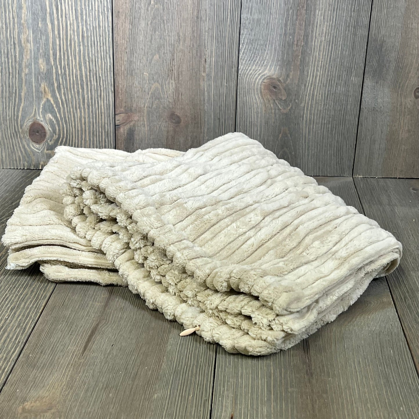 Creamy white striped corduroy velvet pillow cover folded on wooden surface, showcasing plush texture and elegance.