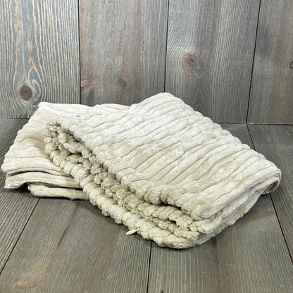 Creamy white striped corduroy velvet pillow cover folded on wooden surface, showcasing plush texture and elegance.
