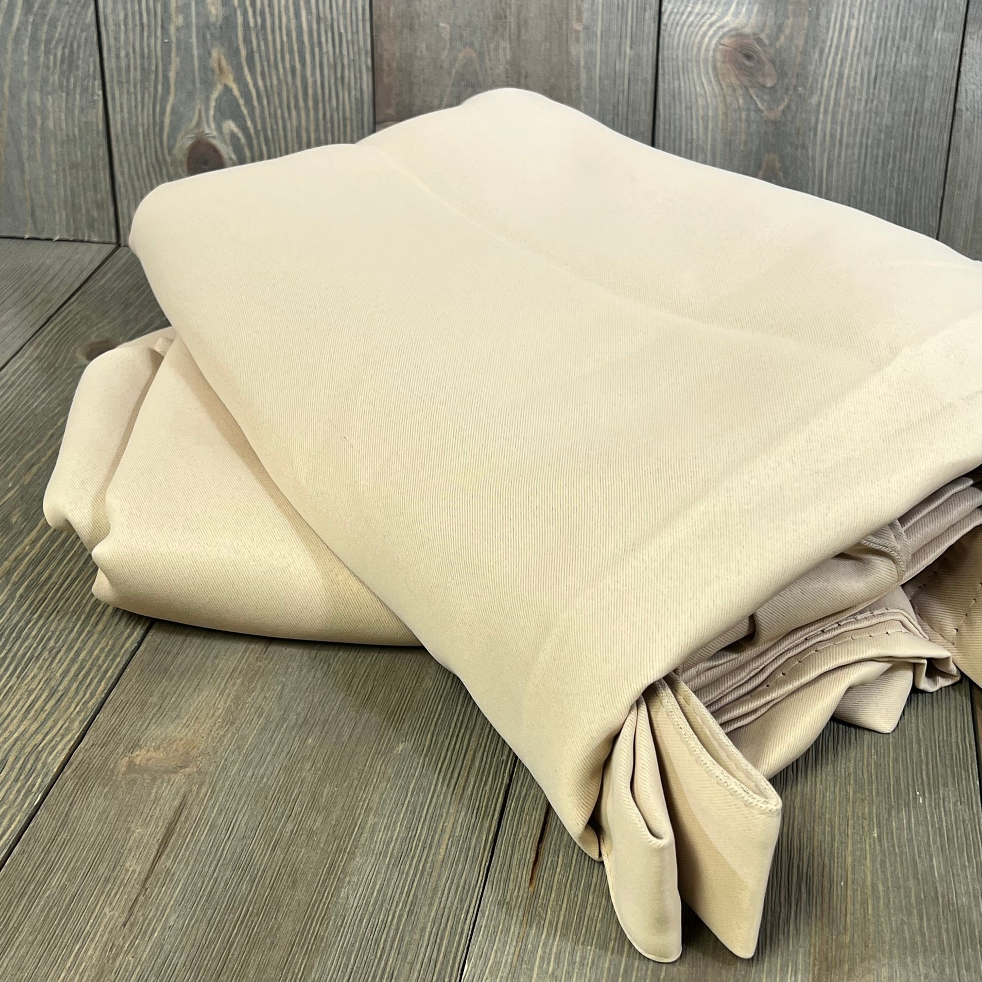 Beige waterproof outdoor curtain panels folded on wooden surface, ideal for gazebo privacy and patio decor.