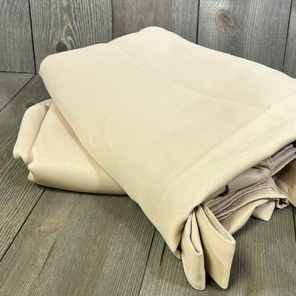 Beige waterproof outdoor curtain panels folded on wooden surface, ideal for gazebo privacy and patio decor.