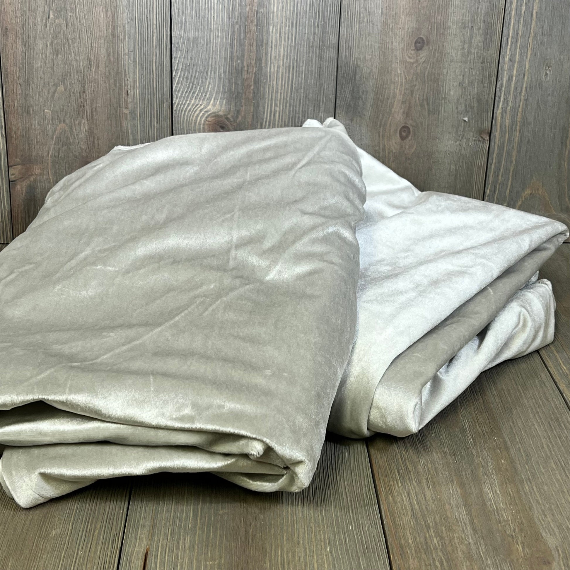 Folded grey blackout curtains on wooden floor, showcasing soft texture and thermal insulation for living rooms and bedrooms.