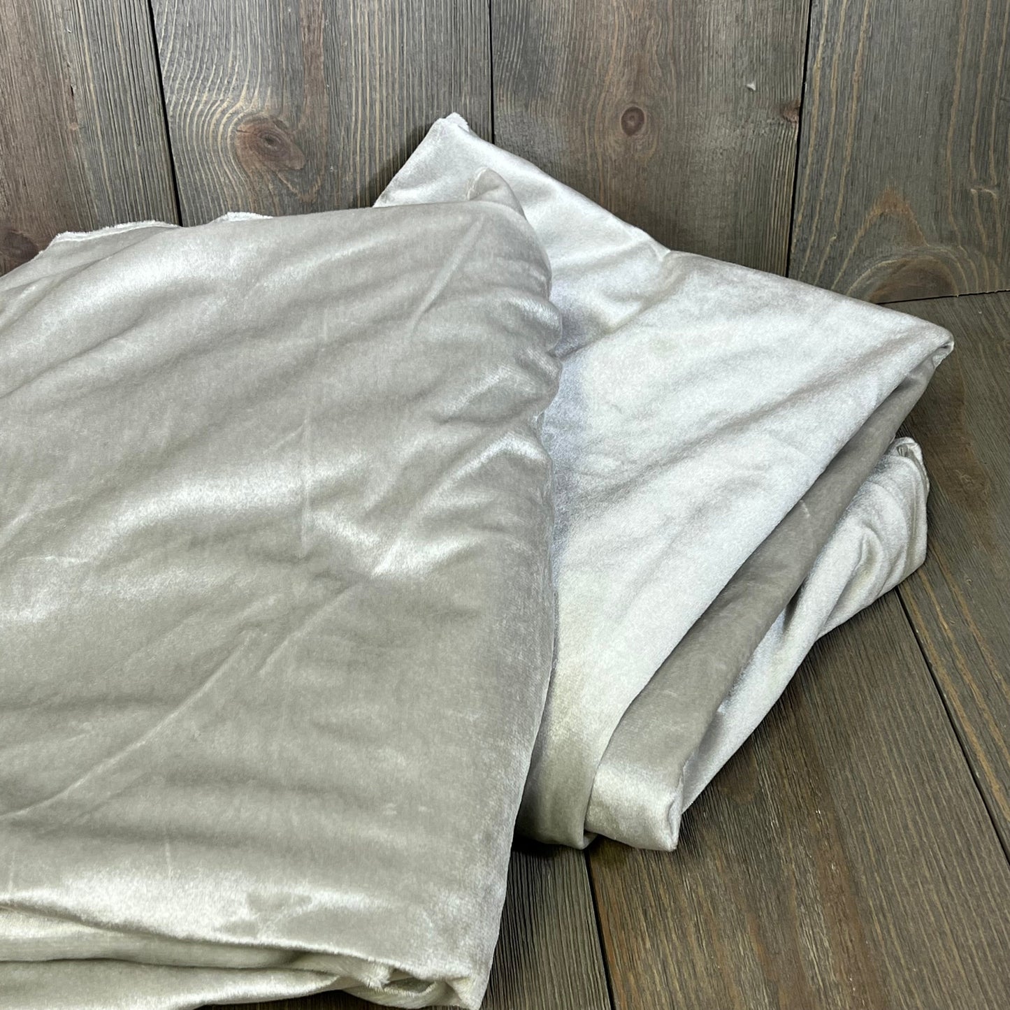 Folded grey blackout curtains on wooden floor, showcasing smooth texture and thermal insulation for living room or bedroom.