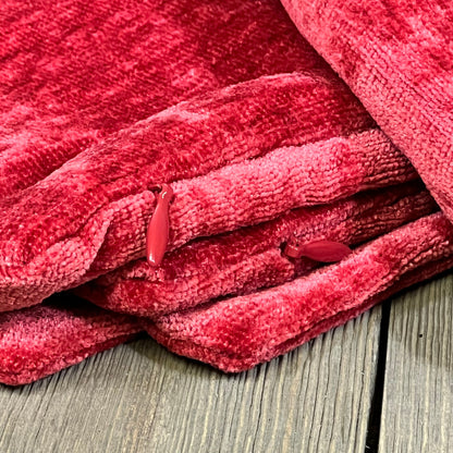 Bright red chenille throw pillow covers stacked on a rustic wooden floor, showcasing soft texture and vibrant color.