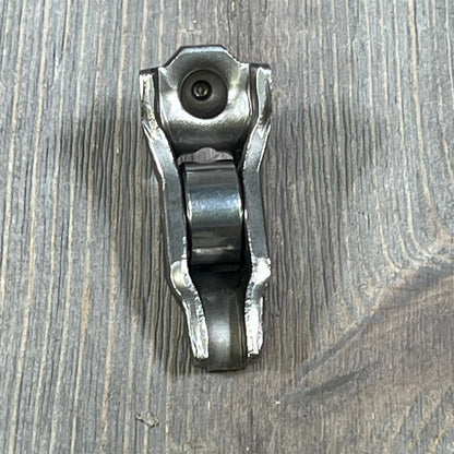 Ford 3L3Z-6564-BA Rocker Arm Valve Assembly on wooden surface, showcasing durable metal construction.