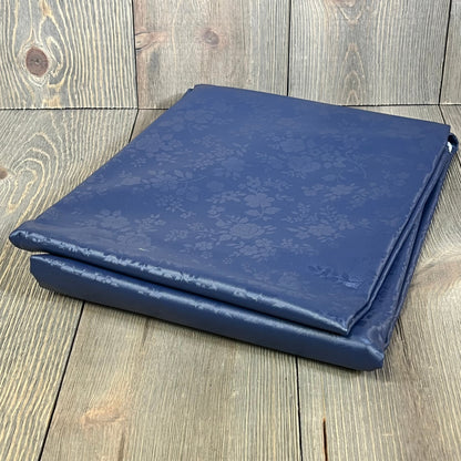 Navy blue waterproof vinyl tablecloth, folded on a wooden surface, showcasing its floral pattern and durable material.