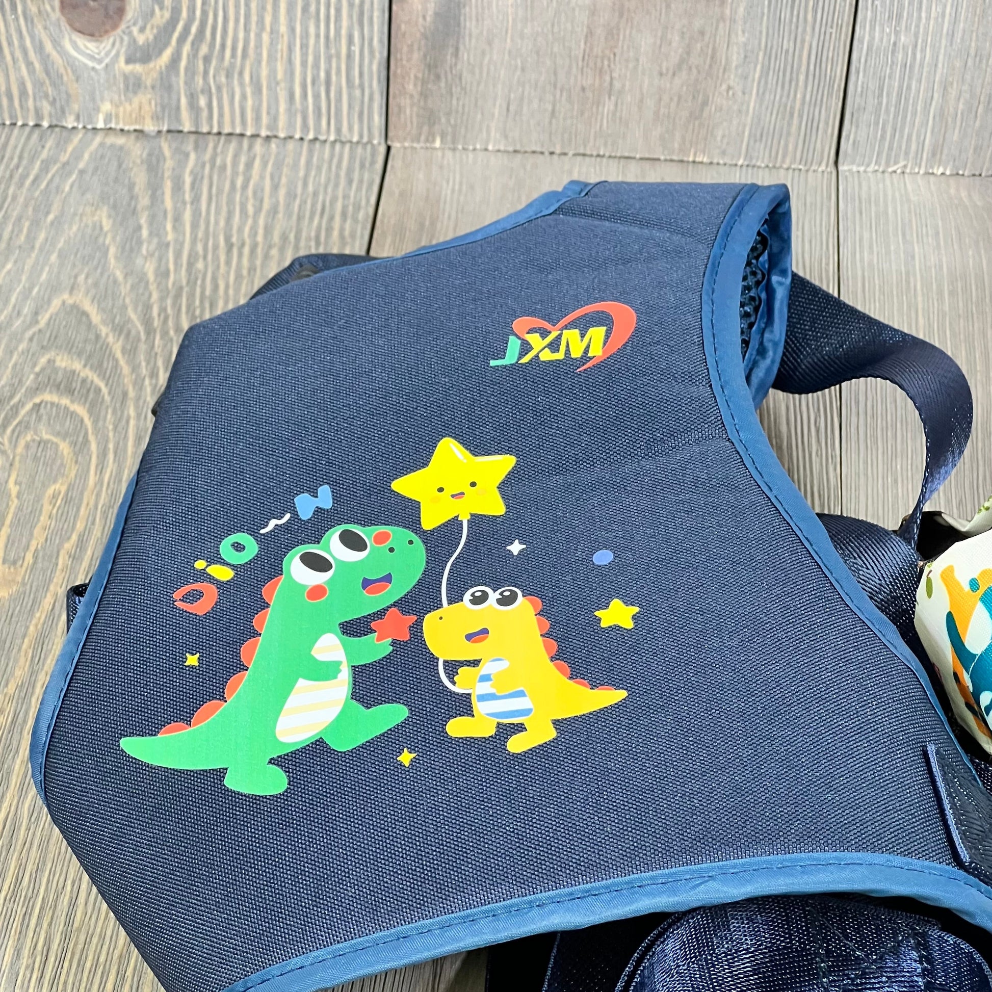 Colorful dinosaur design on safety harness for kids with autism, featuring adjustable straps and light reflector.