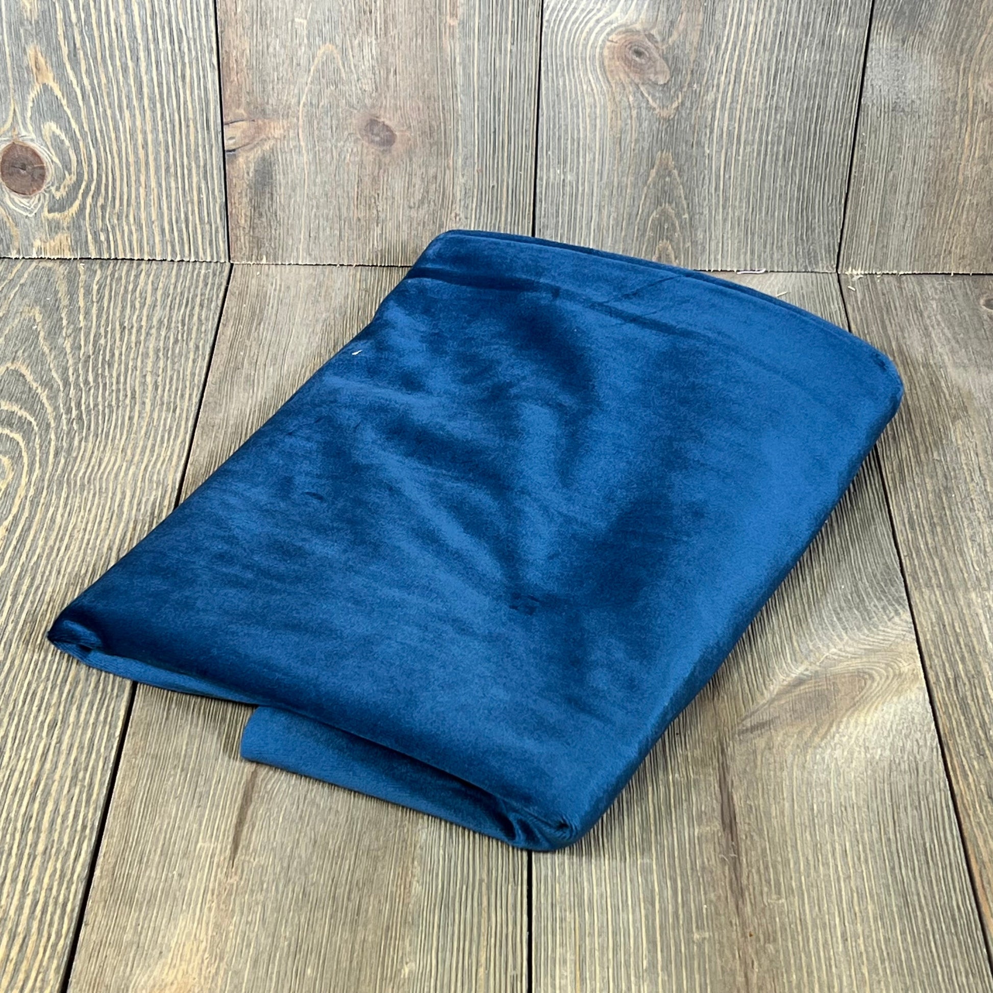 Premium dark blue velvet pillow cover folded on a wooden surface, showcasing its luxurious texture and rich color.