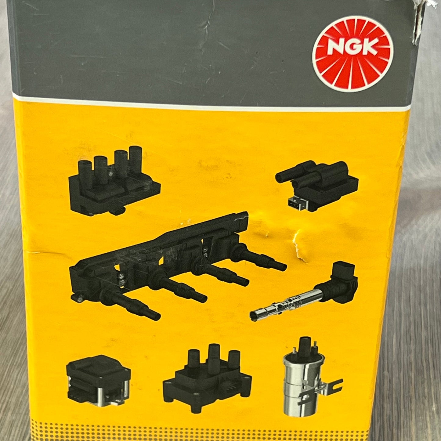 NGK U2029 ignition coil packaging showing various distributorless ignition system components on a yellow background.