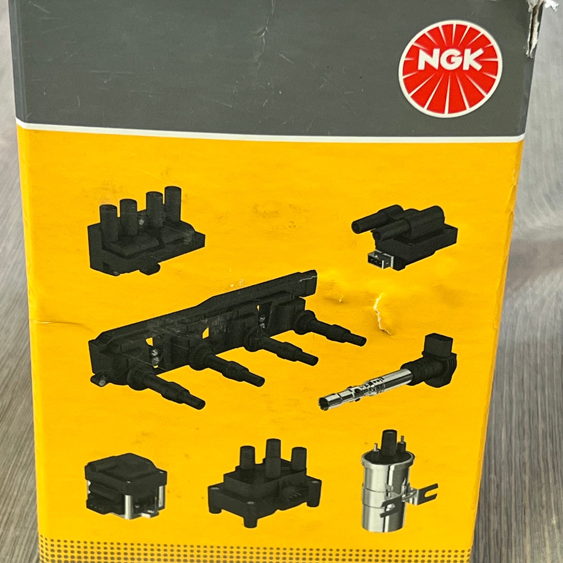 NGK U2029 ignition coil packaging showing various distributorless ignition system components on a yellow background.