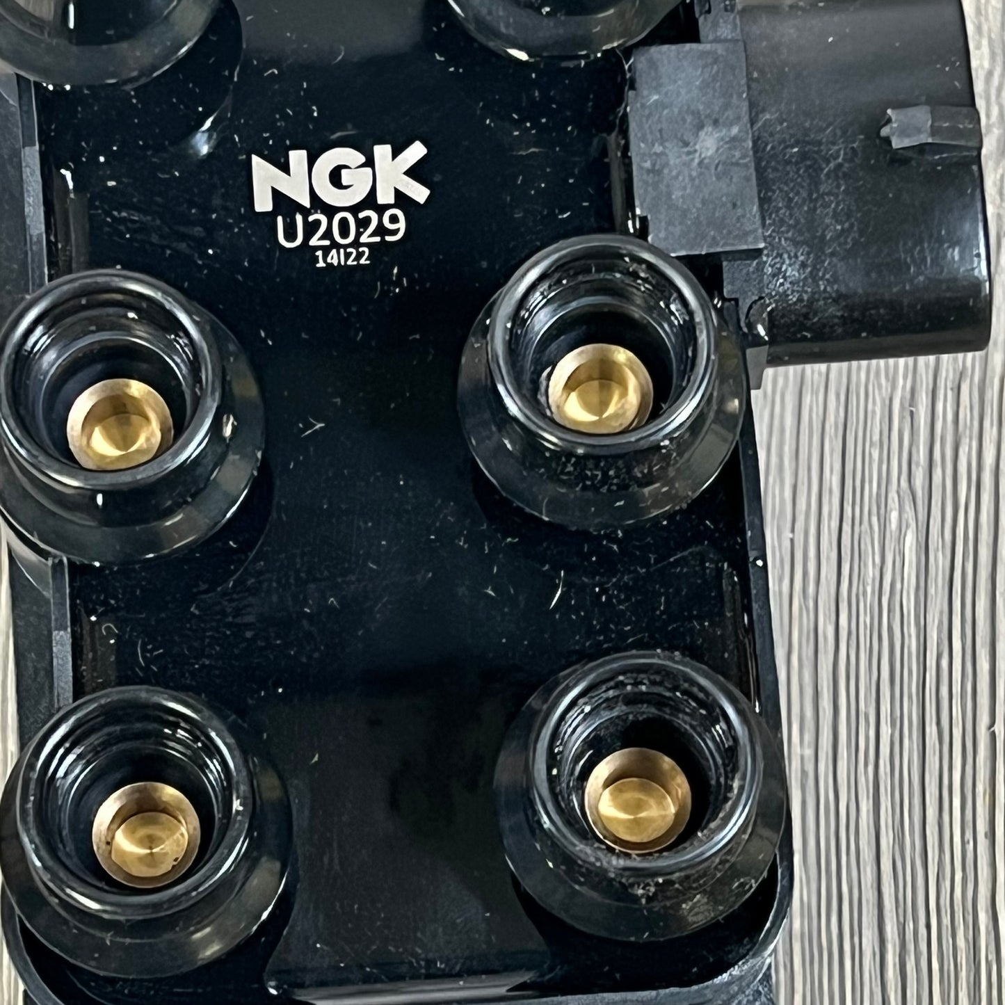 Close-up of NGK U2029 (48806) ignition coil for distributorless systems, showing four brass terminals and black housing.