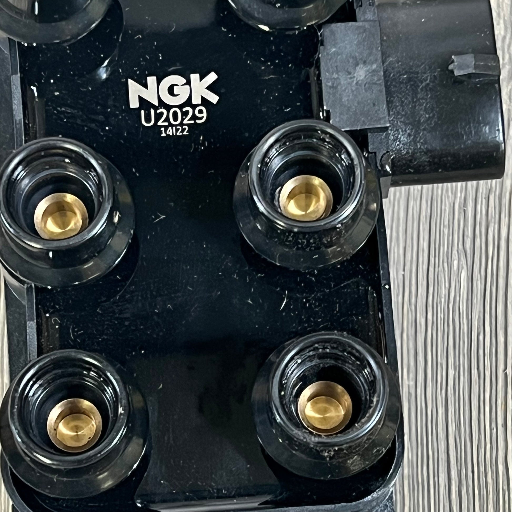Close-up of NGK U2029 (48806) ignition coil for distributorless systems, showing four brass terminals and black housing.
