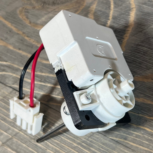 OEM evaporator fan motor for Frigidaire and Kenmore refrigerators with wiring connectors on wooden surface.