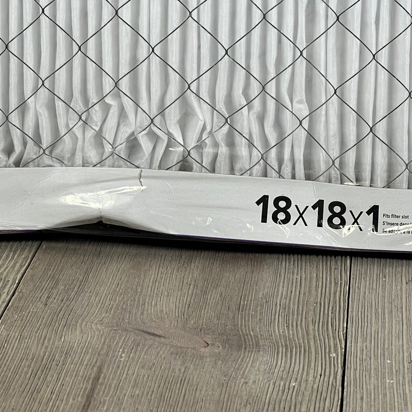 Close-up of Filtrete 18x18x1 MERV 12 air filter, showcasing pleated design and electrostatic material on wood floor.