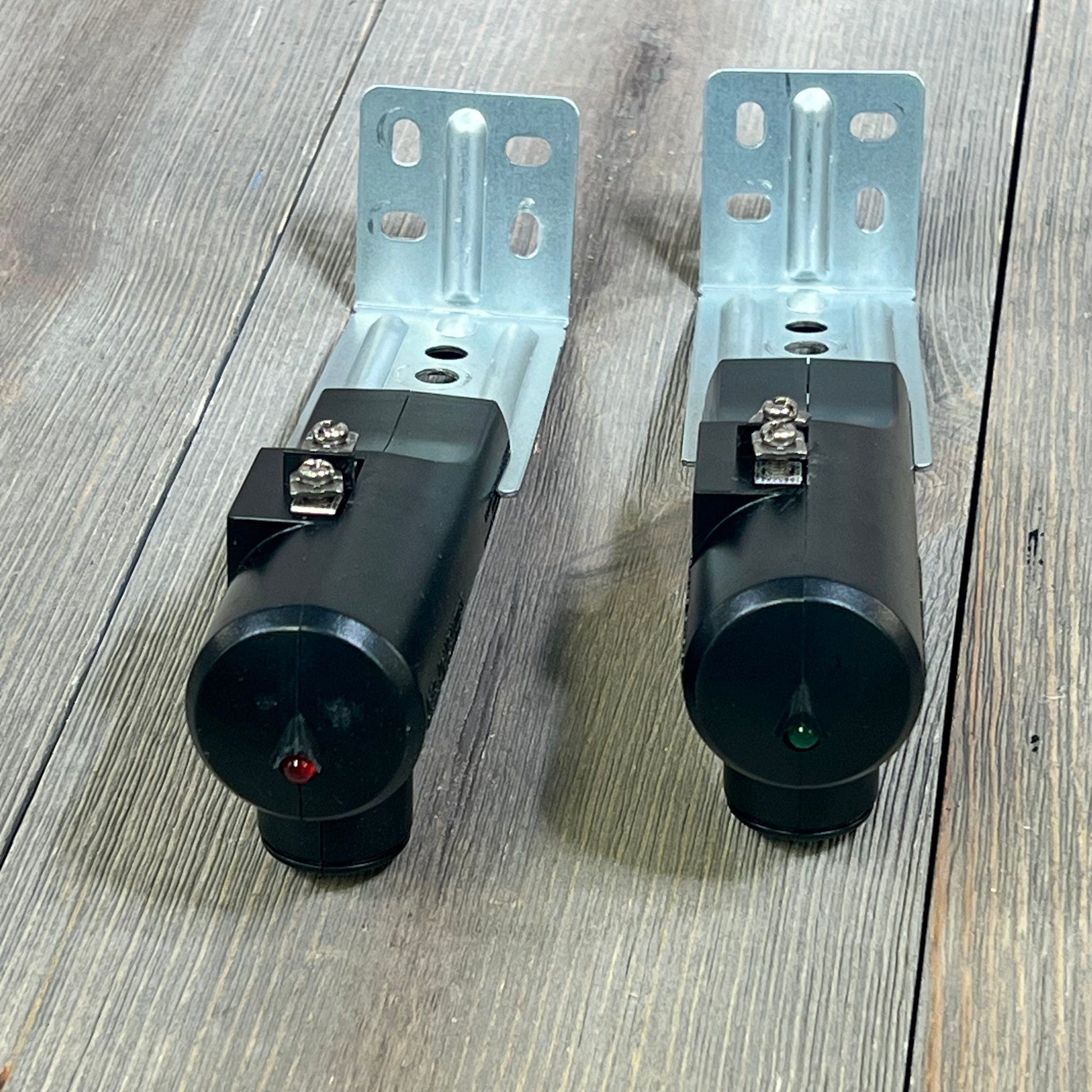 Genie Safe-T-Beam Replacement Kit showing black sender and receiver units with mounting brackets on wood floor.