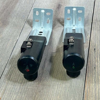 Genie Safe-T-Beam Replacement Kit showing black sender and receiver units with mounting brackets on wood floor.