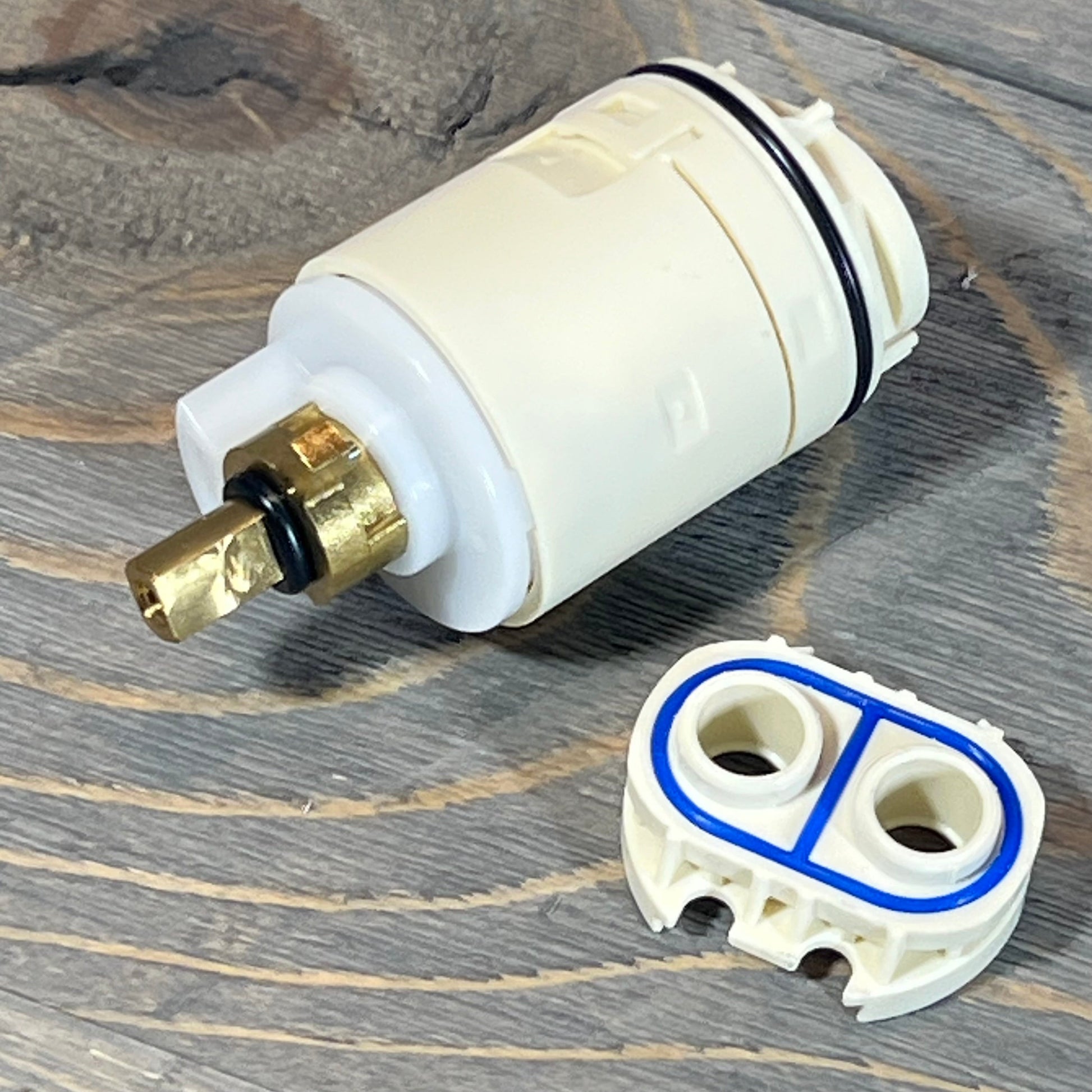 Replacement Peerless shower cartridge and valve assembly on wood surface.